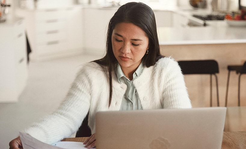 A woman is sitting in front of a computer with papers to prepare for a  home school review