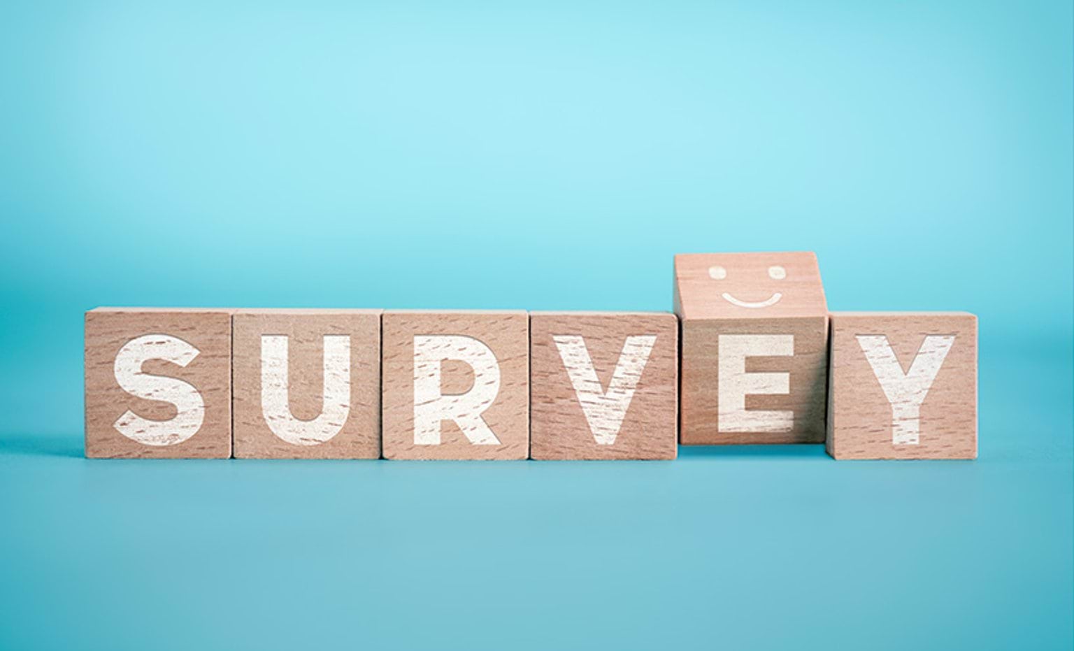 The word "survey" spelled out on wooden cubes, with the letter "e" slightly turned to show a smiley face on top of the cube.
