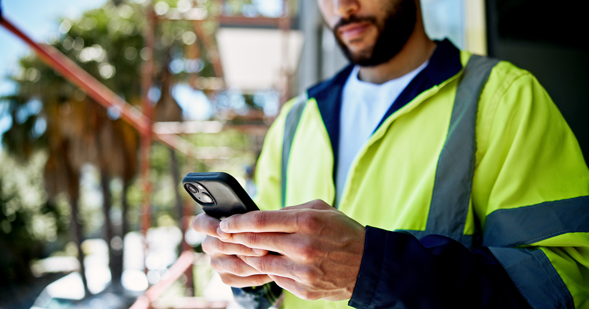 A young man in high-vis gear on a construction site is looking at his phone